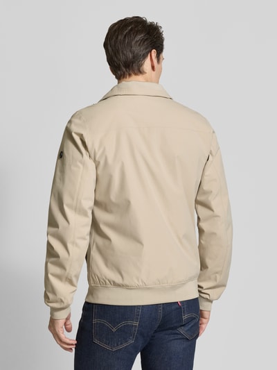 Männermodel trägt Regular Fit Jacke mit Stehkragen Modell 'Alvin' von Didriksons in Beige, glatte Oberfläche, elastische Abschlüsse, Ganzkörperansicht Rückansicht