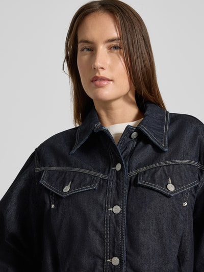 Frauenmodel trägt Regular Fit Jeansjacke aus Baumwoll-Lyocell-Mix Modell 'BOMBER TRUCKER 1.0' von BOSS Orange in dunkler Denim-Optik, Nahaufnahme Oberkörper.