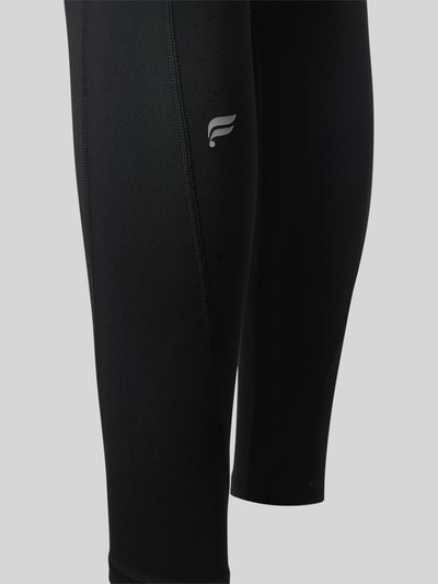 Frauenmodel trägt schwarze Slim Fit Leggins mit Beintaschen Modell 'OASIS' von Fabletics, elastischer Stoff, Detailaufnahme.