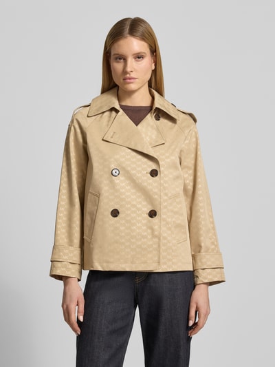 Frauenmodel trägt Trenchcoat mit Logo-Muster von MICHAEL Michael Kors in Beige mit Zweireiher, Reverskragen und Ärmelriegel, Regular-Fit, Ganzekörperansicht von vorne. Rückenlänge bei Größe S: 65 cm, Schulterbreite: 48 cm, Brustweite: 53 cm, Ärmellänge: 57 cm.