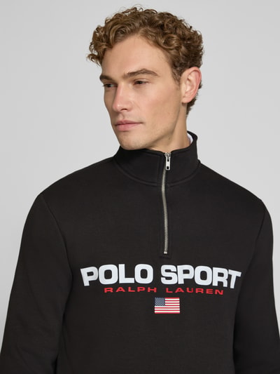 Męski model nosi Relaxed Fit Troyer aus Baumwoll-Mix od Polo Ralph Lauren, kolor czarny z nadrukiem i zamkiem, zbliżenie na górną część ciała.