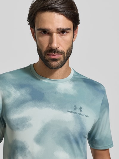 Männermodel trägt T-Shirt im Allover-Look mit Logo van Under Armour, regular fit, rond hals, stretch-mix, allover-patroon, bovenlichaam close-up.