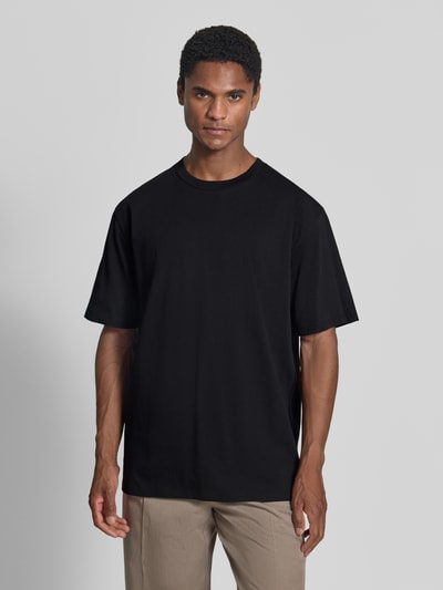 Männermodel trägt Oversized T-Shirt aus reiner Baumwolle von Lindbergh in Schwarz, lockere Passform, halbärmelig, Ganzkörperansicht von vorne, Herren T-Shirt, Rückenlänge Größe M: 70 cm, leicht überschnittene Schultern.