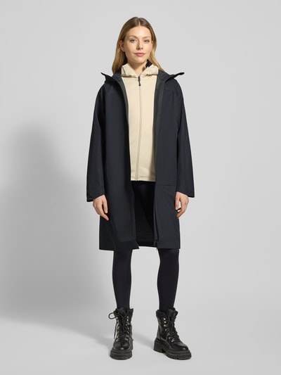 Frauenmodel trägt Mantel mit Zweiwege-Reißverschluss und Kapuze von PEAK PERFORMANCE in Dunkelblau, Relaxed Fit, Ganzkörperansicht von vorne.