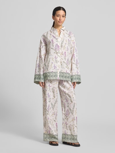 Frauenmodel trägt Florale Leinen Langarmbluse mit Lavendelprint von Christian Berg Woman, weiß mit lila-grünem Blumenmuster, Relaxed Fit, Hemdblusenkragen, kontrastierende grüne Abschlüsse, Ganzkörperansicht von vorne.