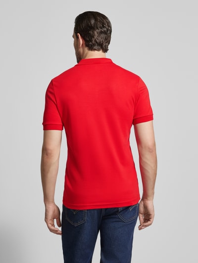 Männermodel trägt Regular Fit Poloshirt aus reiner Baumwolle von Lacoste in Unifarbe Rot mit Logo-Detail, Ganzkörperansicht Rückansicht.