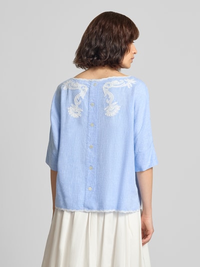 Kobieta modelka nosi Blusenshirt mit Leinen-Anteil und Motiv-Stitching od Christian Berg Woman, jasnoniebieski, mieszanka wiskozy i lnu, krój loose fit, dekolt w łódkę z kontrastową lamówką, wyhaftowany motyw, długość tyłu w rozmiarze 36: 55 cm, długość rękawów w rozmiarze 36: 34 cm, widok całej sylwetki od tyłu.