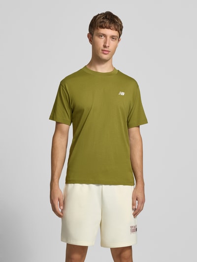Männermodel trägt olivgrünes T-Shirt mit Label-Stitching Modell 'ESSENTIALS' von New Balance, Baumwolle, gerade Form, Ganzkörperansicht von vorne.