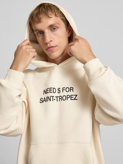 Männermodel trägt Oversized Hoodie aus Baumwoll-Mix Modell 'LEROY' von Only & Sons in Beige mit Statement Print, Nahaufnahme Oberkörper.
