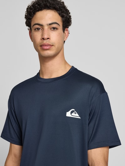 Männermodel trägt T-Shirt mit Rundhalsausschnitt und Logo von Quiksilver, dunkles Blau, Material-Mix mit Stretch-Anteil, Regular-Fit, Nahaufnahme Oberkörper, Rückenlänge bei Größe M: 75 cm.
