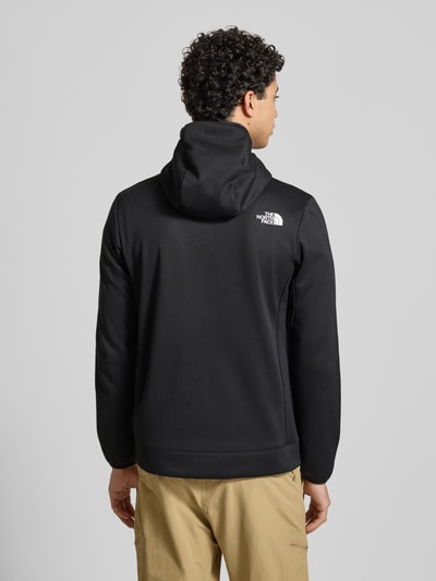 Männermodel trägt Sweatjacke mit Napoleontasche Modell 'MOUNTAIN ATHLETICS' von The North Face in Schwarz, Körpernahe Passform, Kapuze, Label-Details, elastische Abschlüsse, Produktkontext, Ganzkörperansicht Rückansicht