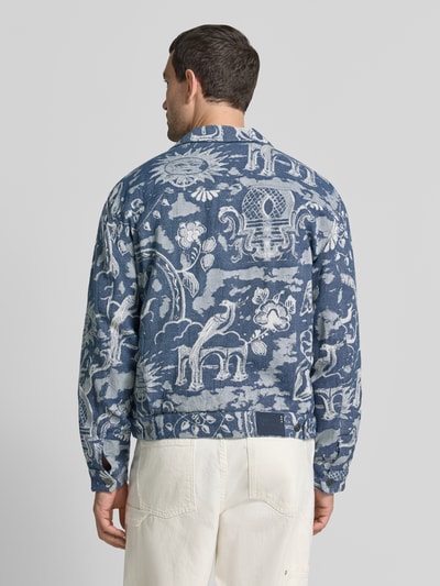 Męski model nosi Jacke im Allover-Look mit Reverskragen od Scotch & Soda we wzór na całej powierzchni, krój regular fit, listwa guzikowa, brustasza, niebieskie i białe kolory, długość tyłu w rozmiarze M: 61 cm, szerokość ramion w rozmiarze M: 43 cm, szerokość w rozmiarze M: 51 cm, długość rękawów w rozmiarze M: 62 cm, widok całej sylwetki od tyłu.