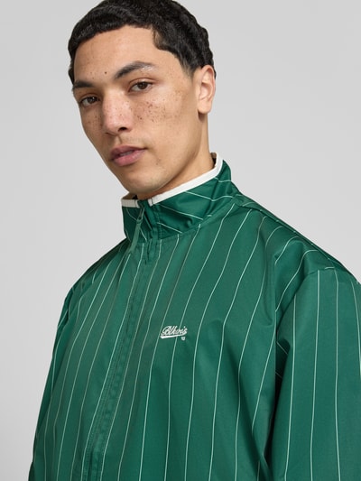 Männermodel trägt Jacke mit Streifenmuster und Reißverschluss von BLKVIS in Grün mit Label-Stitching und Stehkragen, Nahaufnahme Oberkörper.