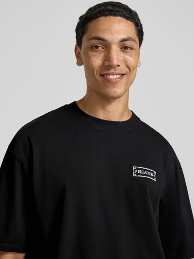 Männermodel trägt zwart oversized fit heren T-shirt van puur katoen, logoprint voor, model 'Viborg' van Pegador, nahaufnahme bovenlichaam.