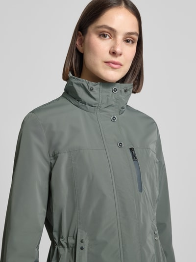 Frauenmodel trägt Funktionsjacke mit Brusttasche von Gil Bret in Grün, mit Kapuze, Stehkragen, Tunnelzug, Nahaufnahme Oberkörper. Rückenlänge 74 cm, Schulterbreite 41 cm, Brustweite 47 cm, Ärmellänge 65 cm bei Größe 36.