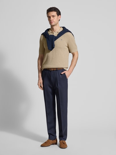 Männermodel trägt Regular Fit Poloshirt mit Label-Stitching von Gant aus reiner Baumwolle in Beige, kombiniert mit dunkler Hose, Ganzkörperansicht von vorne.