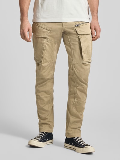 Mężczyzna model nosi Regular Tapered Fit Spodnie cargo z kieszenią zapinaną na zamek błyskawiczny od G-Star RAW, mieszanka bawełny i elastanu, model Rovic, 5 kieszeni, beżowy kolor, szlufki na pasek, widok na całą sylwetkę z przodu.