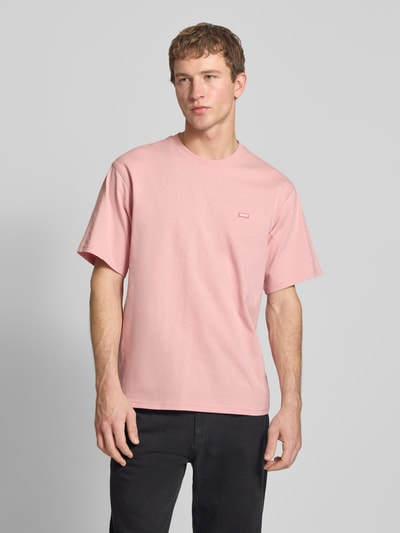 Männermodel trägt T-Shirt mit Label-Detail und Rundhalsausschnitt von Dickies in Rosa, entspannte Passform, Ganzkörperansicht von vorne.