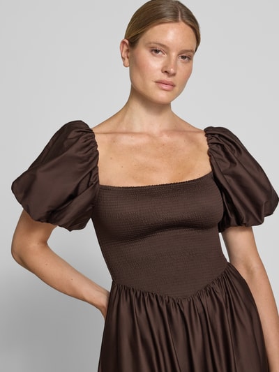Frauenmodel trägt Cocktailkleid mit Smok-Details und Puffärmeln von Jake*s Cocktail in Braun, reine Baumwolle, Nahaufnahme Oberkörper.