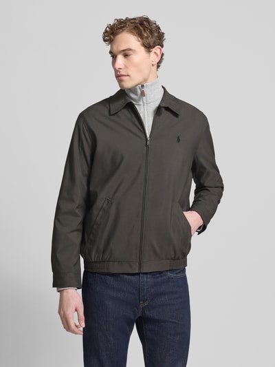 Męski model nosi Kurtkę z wyhaftowanym logo od Polo Ralph Lauren, krój regular fit, kołnierzyk typu kent, zamek błyskawiczny, wpuszczane kieszenie, długość tyłu 68 cm, szerokość ramion 49 cm, szerokość klatki piersiowej 62 cm, długość rękawów 64 cm; kolor ciemny, tekstura gładka, góra z przodu, całkowity widok.