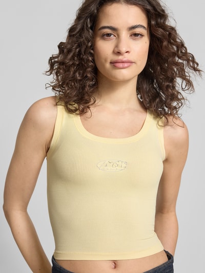 Frauenmodel trägt Slim Fit Top mit Logo-Detail von ANOTHER COTTON LAB, elastischer Baumwoll-Mix, pastellgelb, Rundhalsausschnitt, Nahaufnahme Oberkörper.