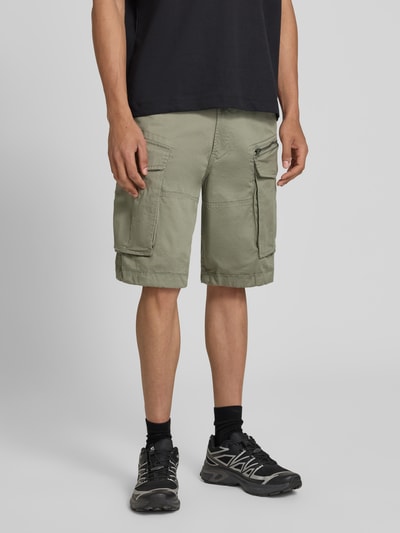 Männermodel trägt bermudy z mieszanki bawełny z dodatkiem streczu model 'ROVIC ZIP' od G-Star Raw, straight fit, kolor khaki, 5 kieszeni, kieszenie z patką i zamkiem błyskawicznym, z tyłu kieszenie z wypustką, szerokość w rozmiarze 32: 44 cm, długość wewnętrzna nogawki: 28 cm, zapięcie na guzik i zamek błyskawiczny, całkowity widok z przodu.