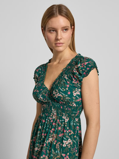 Modelka kobieca nosi Regular Fit Maxikleid aus reiner Viskose mit V-Ausschnitt od Apricot, kwiatowy nadruk na całej powierzchni, obszycie falbanami, taliowany krój, efekt marszczenia, kolor zielony z różowymi i białymi detalami, długość tyłu 129 cm, szerokość w rozmiarze S: 46 cm, dekolt w serek, krótki rękaw, wiskoza, kwiatowa tekstura, zbliżenie na górną część sylwetki