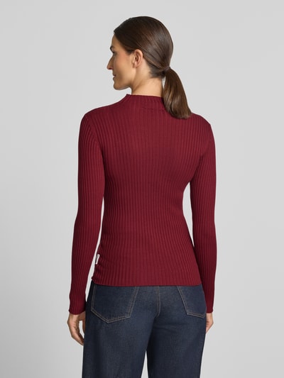 Frauenmodel trägt dunkelroten, gerippten Slim Fit Pullover aus reiner Baumwolle Modell 'ALAANIA' von ARMEDANGELS, Ganzkörperansicht Rückansicht. Damen Pullover von ARMEDANGELS.