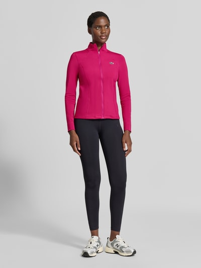 Frauenmodel trägt Slim fit Trainingsjacke mit Logo-Patch von Lacoste in Pink und Schwarz, glatte Struktur, Damen Trainingsjacke, Ganzkörperansicht von vorne.