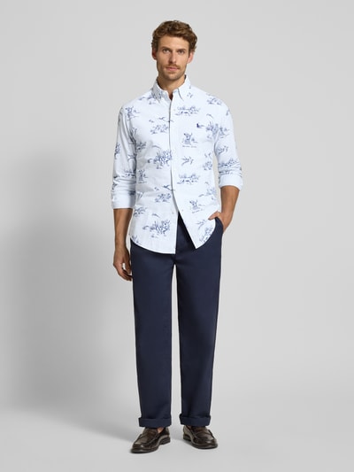 Männermodel trägt Custom Fit Freizeithemd aus reiner Baumwolle von Polo Ralph Lauren mit blauem Muster auf weißem Stoff, dunkle Hose, Ganzkörperansicht von vorne.