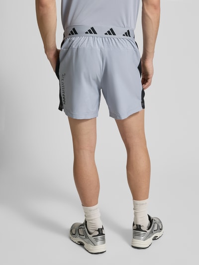 Männermodel trägt Regular Fit Sport-Shorts aus schnelltrocknendem Material von adidas Training, Mehrfarbig, Schriftzug, perforierte Einsätze, elastischer Bund, seitliche Eingrifftaschen, Rückansicht Ganzkörperansicht.