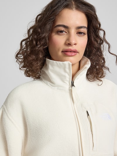 Frauenmodel trägt Fleecejacke mit Stehkragen und Label-Stitching von The North Face in Offwhite, Textur soft, Brusttasche, Nahaufnahme Oberkörper. Regular Fit, Reißverschluss, Kontext Damen Fleecejacke.