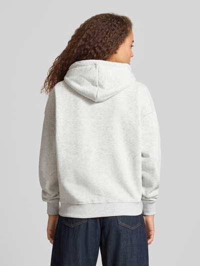 Männermodel trägt Oversized Fit Sweatjacke mit geteilter Kängurutasche von Gina Tricot aus mieszanka bawełny w kolorze jasnoszarym, elastyczne wykończenia, kaptur z tunelem, Ganzkörperansicht Rückansicht.