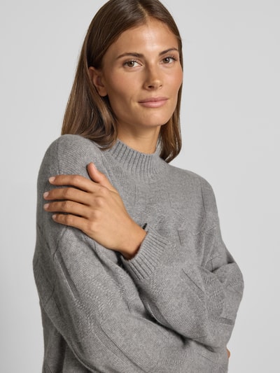 Frauenmodel trägt Oversized Wollpullover mit Kaschmir-Anteil von Emporio Armani, graues Strukturmuster, Stehkragen, Nahaufnahme Oberkörper.