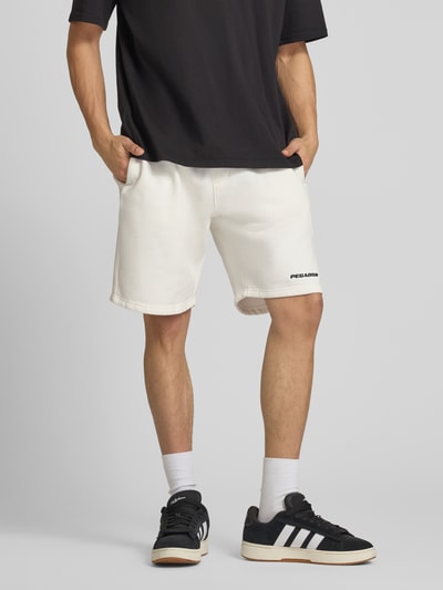 Męski model nosi szorty z mieszanki bawełny, krój loose fit, elastyczny pas, wpuszczane kieszenie, wyhaftowane logo, Pegador. Ganzkörperansicht von vorne.