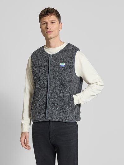 Männermodel trägt Straight fit bodywarmer met logopatch model 'Hoktown' van American Vintage in imitatiebont, donkergrijs, knoopsluiting, ronde hals, ruglengte 64 cm, schouderbreedte 44 cm, borstwijdte 62 cm, ganzkörperansicht van voren.