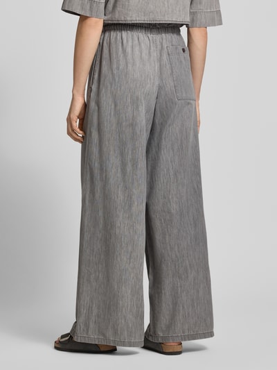 Kobieta modelka nosi spodnie materiałowe Wide Fit Stoffhose mit Rüschenbesatz Modell 'Dwindle' od Drykorn z czystej bawełny, krój wide fit, obszycie falbanami, elastyczny pas z tunelem, wpuszczane kieszenie, szerokość w rozmiarze 27/34: 37 cm, długość wewnętrzna nogawki: 82 cm, szary melanż, tył całej sylwetki.