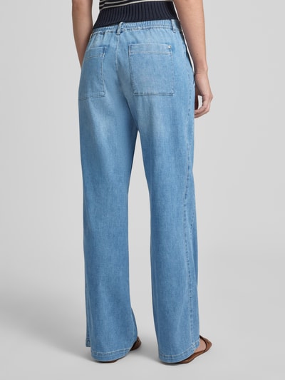 Frauenmodel trägt Wide Leg Jeans mit elastischem Bund von Brax im Used-Look, hellblaue Denim-Struktur, Ganzkörperansicht Rückansicht.