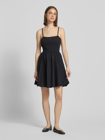Frauenmodel trägt Tailliertes Freizeitkleid aus reiner Baumwolle von Tommy Jeans, unifarben in Schwarz, Mini-Länge, Logo-Stitching, Spaghettiträger, seitliche Eingrifftaschen, gerade Textur, U-Ausschnitt, Ganzkörperansicht von vorne.