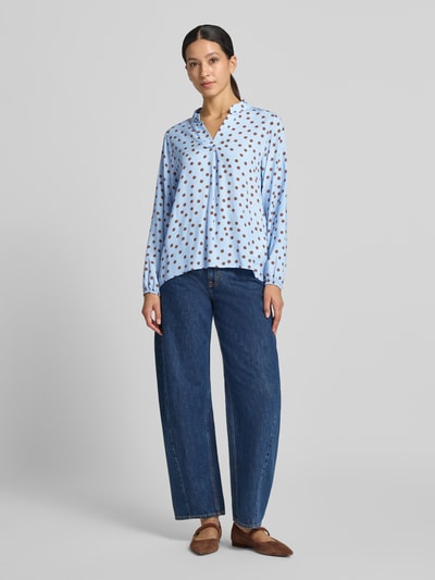 Frauenmodel trägt Relaxed Fit Bluse aus reiner Viskose-Mix Modell 'Valeria' von ZABAIONE, blau mit braunen Punkten, Ganzkörperansicht von vorne. Damen Bluse, Serafino Ausschnitt, langärmelig, Rückenlänge 54 cm, Ärmellänge 58 cm
