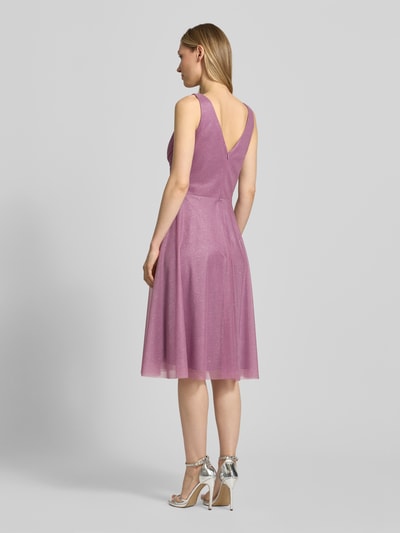 Frauenmodel trägt schimmerndes Knielanes Cocktailkleid mit V-Ausschnitt von TROYDEN COLLECTION aus Mesh, Taillierter Schnitt, Drapierungen, Ganzkörperansicht Rückansicht. Rückenlänge 88 cm, Brustweite 36 cm bei Größe 36.