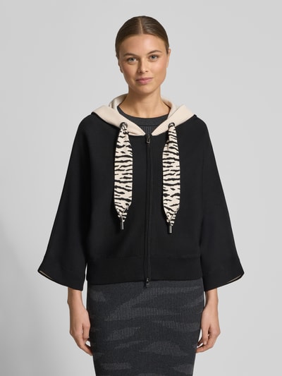 Vrouwenmodel draagt Strickjacke mit Reißverschluss van Marc Cain, zwart met beige capuchon en tunnelkoord, viscosemix, relaxte pasvorm, driekwartmouwen, geribde boorden, vooraanzicht volledige lichaamsopname.