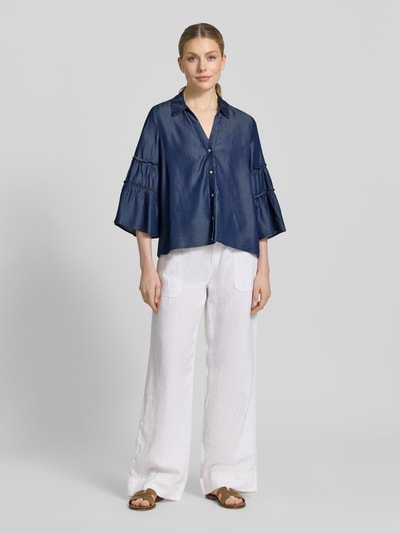 Frauenmodel trägt Regular Fit Jeansbluse aus Lyocell von s.Oliver BLACK LABEL, Denim-Optik, Hemdblusenkragen, Frill-Detail, Langarm mit Trompetenärmel, V-Ausschnitt, einreihige Knopfleiste, glatte Textur, Ganzkörperansicht von vorne.
