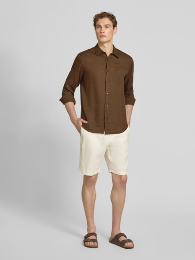 Männermodel trägt Regular Fit Leinenhemd mit kentkraag en borstzak van guess in bruin, gecombineerd met lichte korte broek; heren, zuiver linnen, regular fit, kentkraag, borstzak, ruglengte maat M 77 cm, schouderbreedte 43 cm, mouwlengte 67 cm; ganzkörperansicht von vorne.