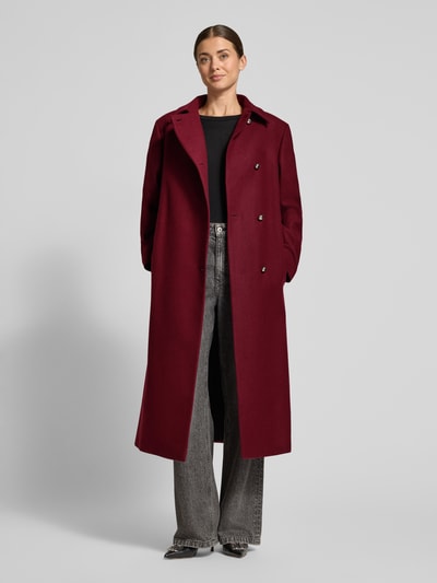 Frauenmodel trägt Mantel mit Bindegürtel Modell 'Melm' von HUGO in dunklem Rot, unifarben, Longline, Zierknöpfe, Gehschlitz, Ganzkörperansicht von vorne.