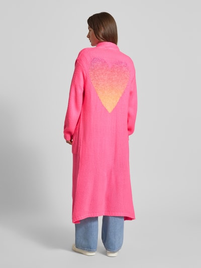 Frauenmodel trägt Longcardigan mit Eingrifftaschen von miss goodlife aus Baumwoll-Alpaka-Mix in Pink mit Herzmuster, lockerer Schnitt, Rückansicht, Ganzkörperansicht.