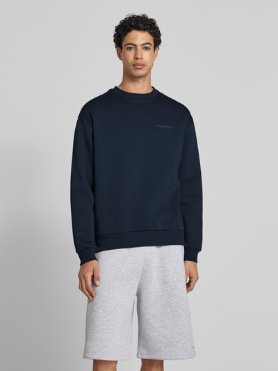Męski model nosi Sweatshirt mit Rundhalsausschnitt und Logo od REVIEW w kolorze granatowym, mieszanka bawełny, krój regular fit, logo, długość tyłu w rozmiarze M: 70 cm, długość rękawów: 62 cm, widok całej sylwetki od przodu