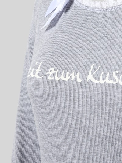 Vrouwenmodel draagt Nachthemd aus Baumwoll-Mix Modell 'Winterzauber' van LOUIS & LOUISA, grijze ribstructuur, statementprint, ruches, strikapplicatie, ronde hals, lang mouw, mix van katoen en elastaan, rechte fit, detailopname bovenlichaam.