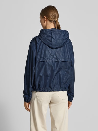 Männermodel trägt Regular Fit Windbreaker mit Kapuze von Tommy Hilfiger, granatowy, wzór logo, elastyczne mankiety, widok całej sylwetki z tyłu