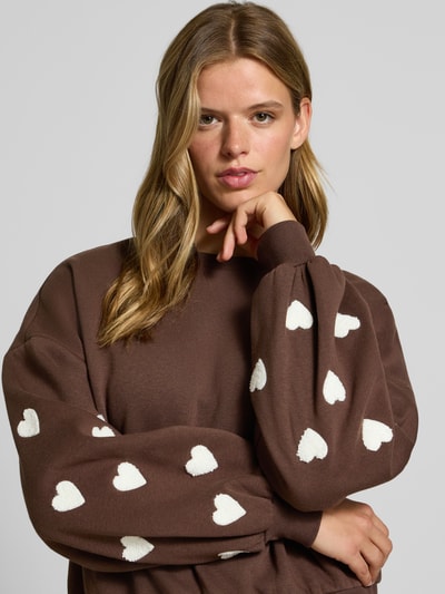 Vrouwenmodel draagt Regular Fit Sweatshirt aus Baumwoll-Mix model 'MACY' van ONLY in bruin met witte hartjes, Dames sweatshirt, Nahaufnahme bovenlichaam.